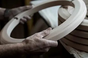 Hände eines Handwerkers halten einen sorgfältig bearbeiteten Holzring, der Teil eines Stressless Sessel-Untergestells ist. Im Hintergrund liegen weitere Holzringe gestapelt.
